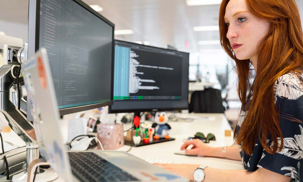 Woman working on a desk with a laptop an 2 external monitors