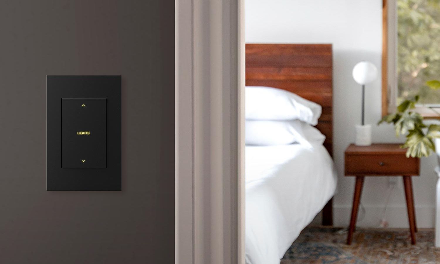 A minimalist lighting control panel on a wall outside a modern bedroom with a wood headboard and crisp white bedding.